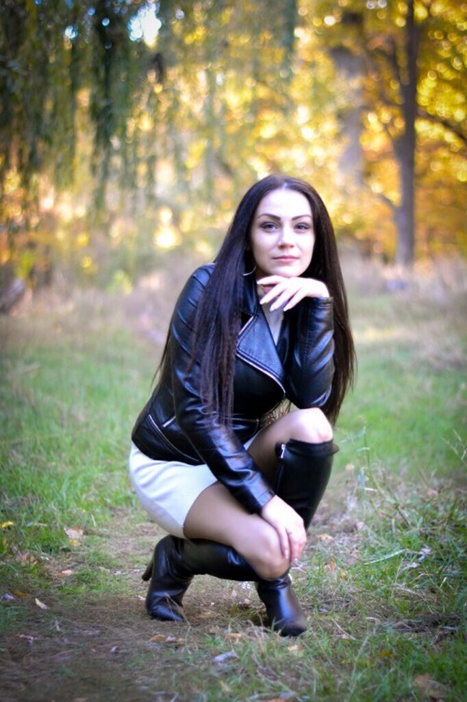 AI caption: a woman in black leather jacket crouching in the woods, portrait