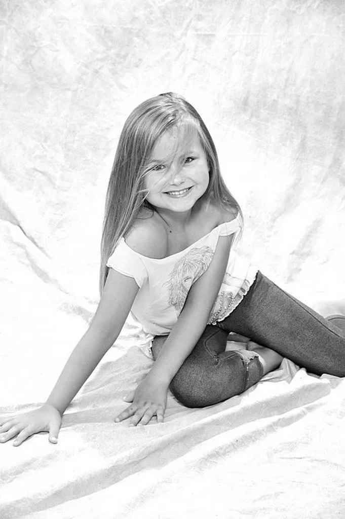 AI caption: a young girl with her hands on her face, portrait a young girl sitting on a white background, the girl is posing in a sexy pose, portrait a little girl posing on a white blanket, the girl is posing in a sexy pose