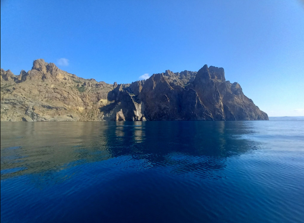 AI caption: a blue ocean with a rocky cliff in the background, panoramic